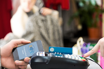 Man completing mobile Payment at Store Cashiers Desk with Terminal