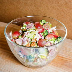 Fresh salad with bacon, grapes, walnuts, greens and herbs and olive oil in transparent glass salad-bowl. Portion of salad on the background of cardboard with space for your text.