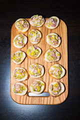 Wooden tray of appetizers on pallet coffee table at banquet with bacon, green herbs and olives.