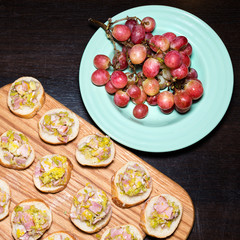 Wooden tray of appetizers on pallet coffee table at banquet with bacon, green herbs and turquoise ceramic plate with grapes.