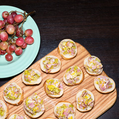 Wooden tray of appetizers on pallet coffee table at banquet with bacon, green herbs and turquoise ceramic plate with grapes.