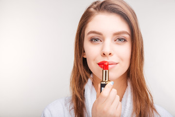 Beautiful smiling young woman in bathrobe using red lipstick