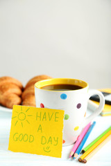 Piece of note paper with cup of coffee and croissant on blue woo