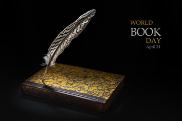 Feather standing on an old book against a black background, text World Book Day