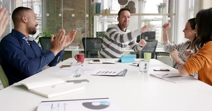 Diverse business people clapping in Creative team meeting celebrating success in casual modern office boardroom with natural light and large open windows