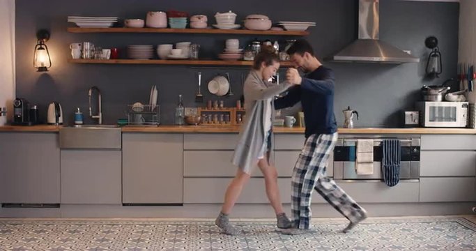 Happy young couple newly wed dancing listening to music in kitchen wearing pajamas coffee morning at home
