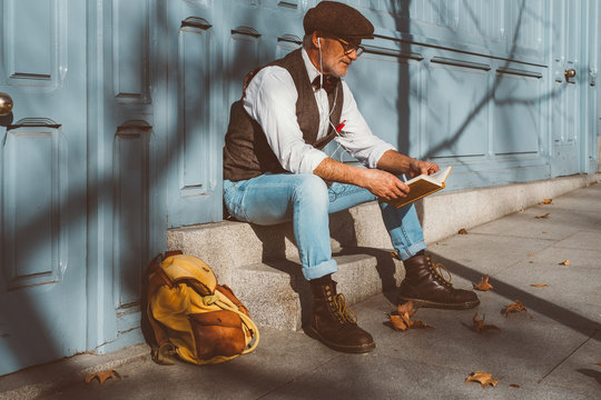 Reading elderly man sitting on the street