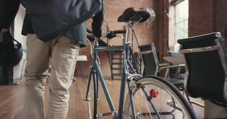 Young businessman arriving at work pushing bicycle carrying helmet - Powered by Adobe