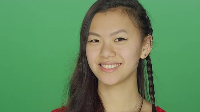 Young Asian woman smiling and being playful, on a green screen studio background