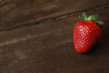 Red ripe strawberry on dark brown wooden background, close-up