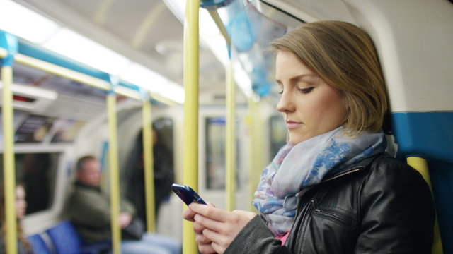 Young woman on a subway train uses her phone whilst standing