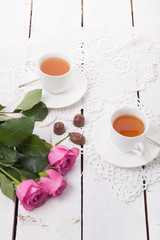 Pink roses tulips with cups of tea and chocolates on vintage nap