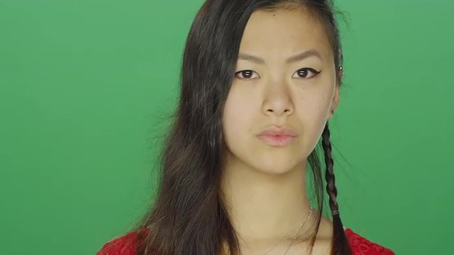 Young Asian woman staring and looking serious, on a green screen studio background