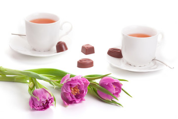 Pink tulips with cups of tea and chocolates isolated