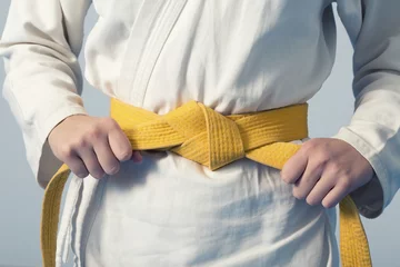 Foto op Plexiglas Vechtsport Handen die gele riem aanhalen op een tiener gekleed in kimono voor vechtsporten