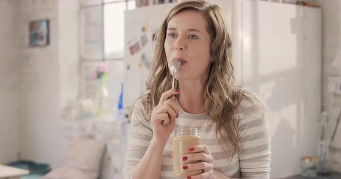 Caucasian girl indulging eating peanut butter from jar using spoon at home in the morning
