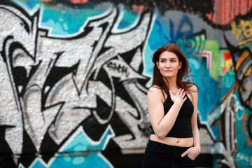 Fototapeta na wymiar Beautiful girl with red hair and belly button piercing standing in front of a wall with graffiti