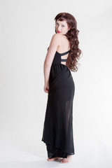 Young lady standing with a long black dress and long curly hair
