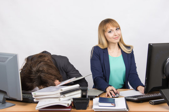 Female colleagues in the office, one had fallen asleep on a pile of folders, the other works in the computer and looked in the frame