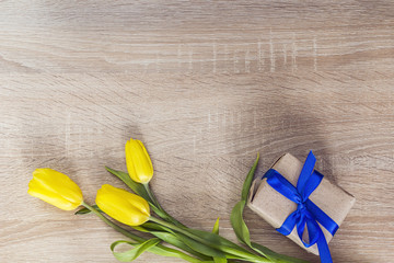Yellow tulips and gift box with blue ribbon on a wooden backgrou