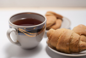 Cup of tea with pattern and fresh croissants