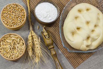 Dough, flour, twig wheat grain oats and wheat grain in wooden bo