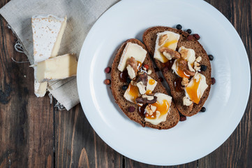 Melted brie with honey, pine nuts and walnuts on dark bread © voloshin311