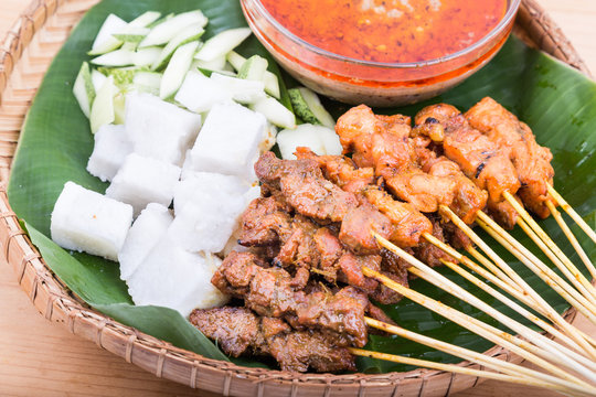 Closeup on freshly barbecue chicken and beef satay with gravy, rice, cucumber and onion served on traditional rattan weaved plate with banana leaf