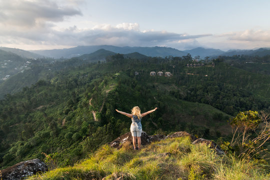 Woman standing at the edge of a hill overlooking green valley in Ella, Sri Lanka