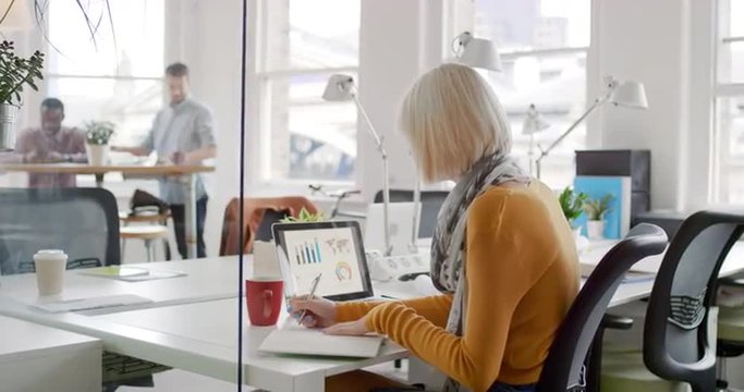 Young business woman working at shared desk in trendy hipster start up office using big data on laptop computer