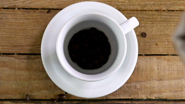 Pouring coffee beans into a cup on an old wooden table, top view