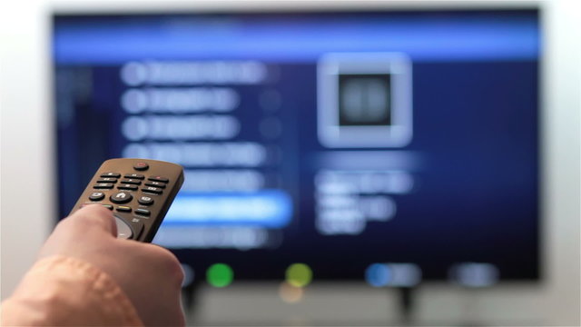 Television remote control changes channels thumb on smart TV screen.