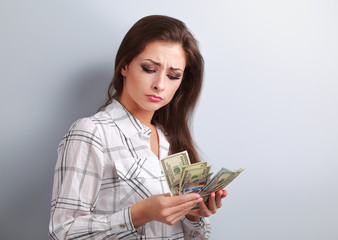 Beautiful young unhappy woman looking on dollars and thinking ho