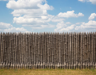 Fototapeta premium Wooden fence with pointed tips on a background of blue sky with