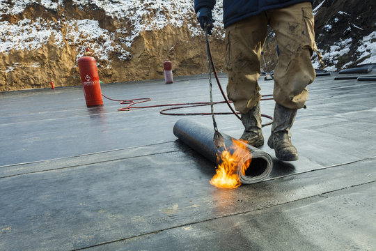 Waterproofing Roll Bituminous Material In The Trench. Construction Worker Manufacturer Uses A Gas Burner Propane Tank Fire.