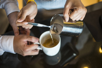 Waitress hands pouring milk making cappuccino