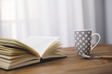 Cup of coffee with a book on wooden table.