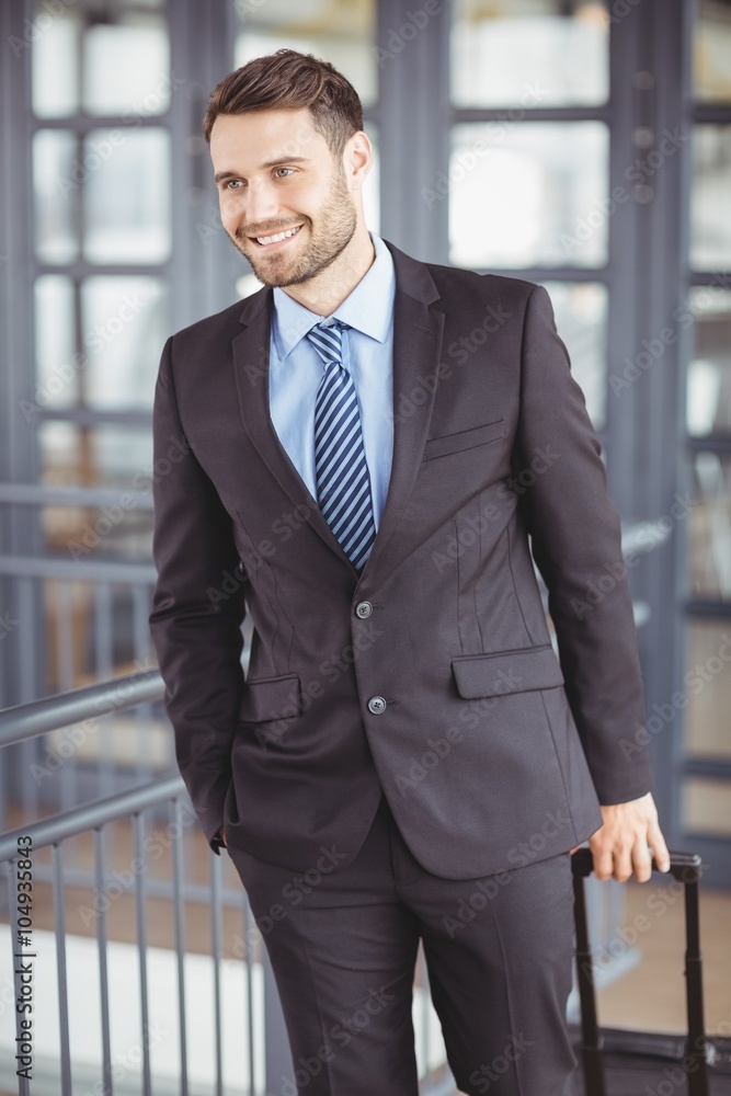 Wall mural handsome businessman walking with luggage by railing