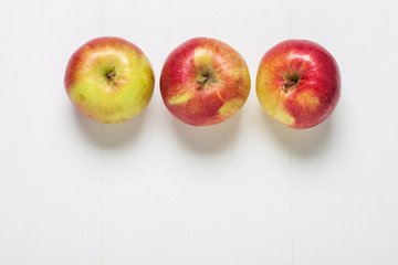 Three fresh apples, top view on white wooden background