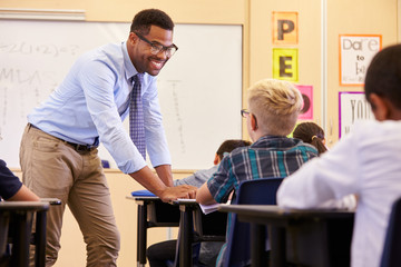 Fototapeta premium Smiling teacher leaning on elementary school pupil’s desk