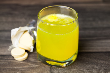 Glass with tablet in water with bubbles on wooden background