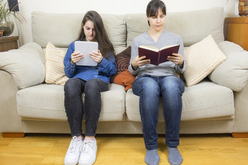 Mother and daughter reading a book and a tablet
