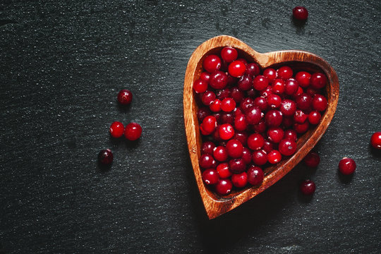 Fresh cranberries in a wooden bowl in the shape of a heart on a