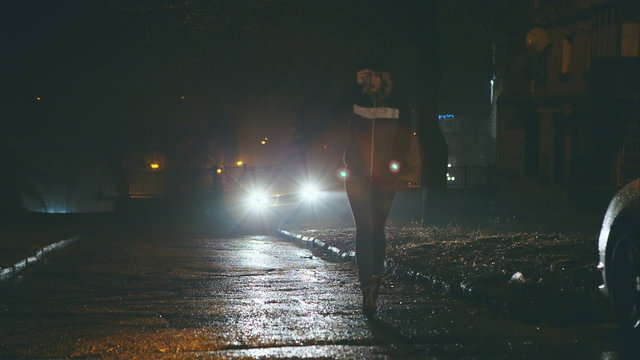 Girl at night is on the dangerous streets of the city on the car headlights.