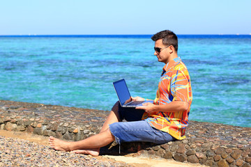 young man, freelancer, working at his laptop computer at the sea 
