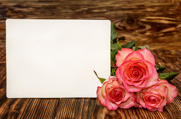 Three roses with blank greeting card on a wooden background
