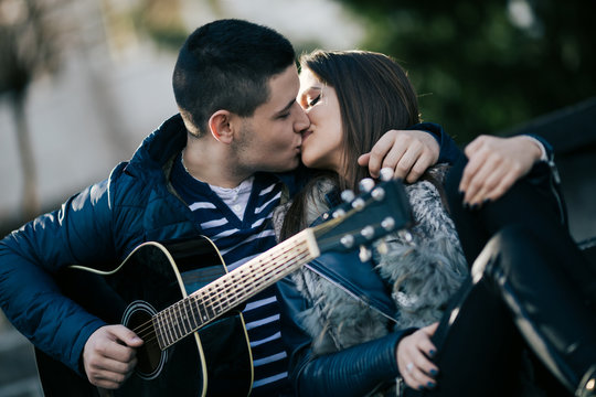 Teenagers lifestyle. Boyfriend with his girlfriend enjoying outdoors, kissing and play the guitar. Outdoor, urban photography.