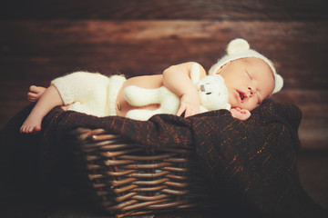 Cute newborn baby in bear hat sleeps in basket with toy teddy be