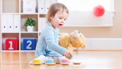 Toddler girl have tea with her teddy bear