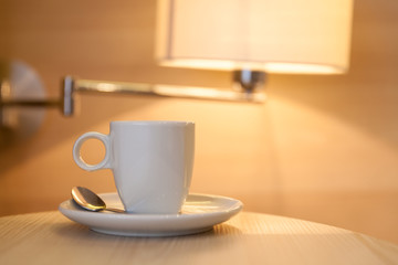 cup of coffee on wooden table at the hotel with a lamp in the ba